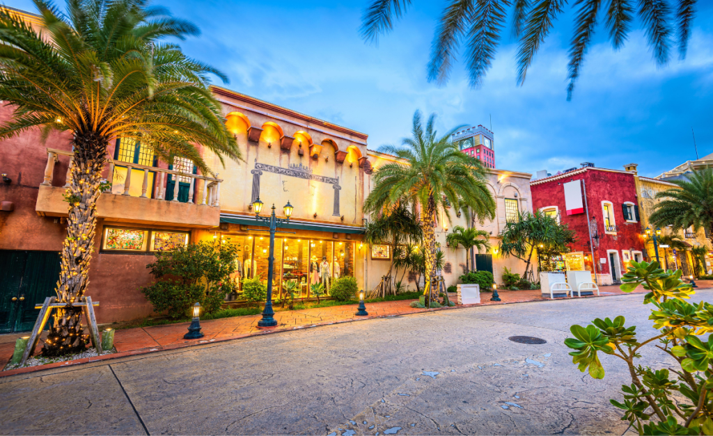 A street with colorful buildings, old fashioned lampposts and palm trees at dusk.